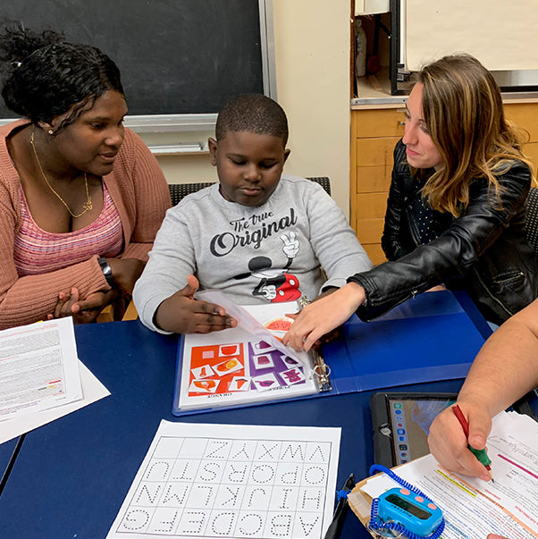 Adults and boy sitting at a table while interacting with learning material