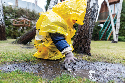 Boy playing in mud on a rainy day, wearing a poncho