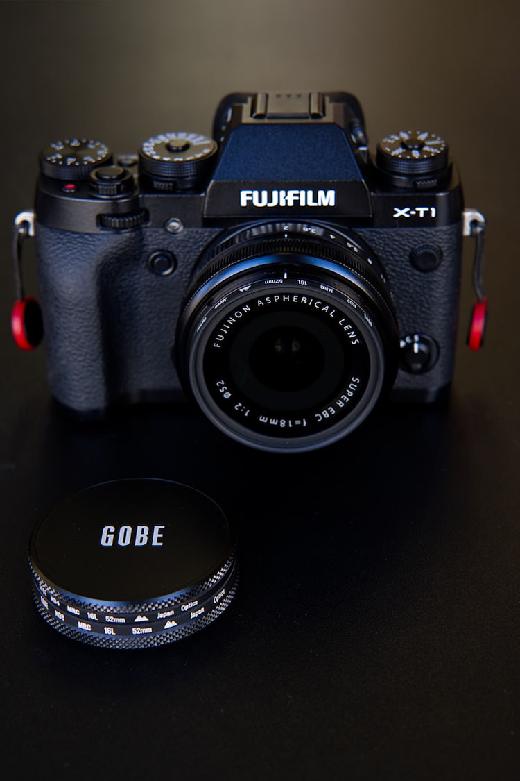 A Fujifilm DSLR with 18mm prime lens standing next to two different ND filters