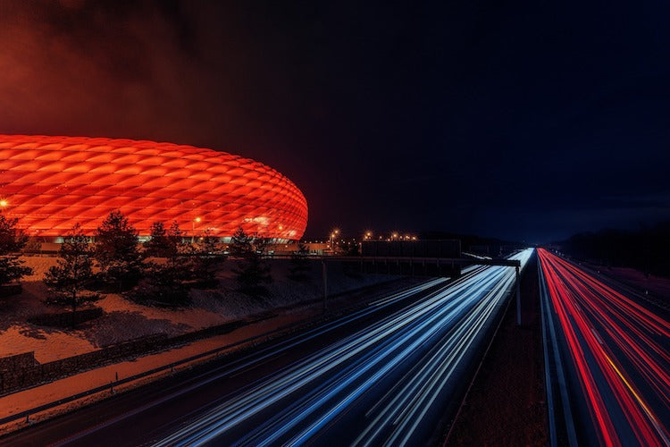 cars passing next to Allianz Arena at night