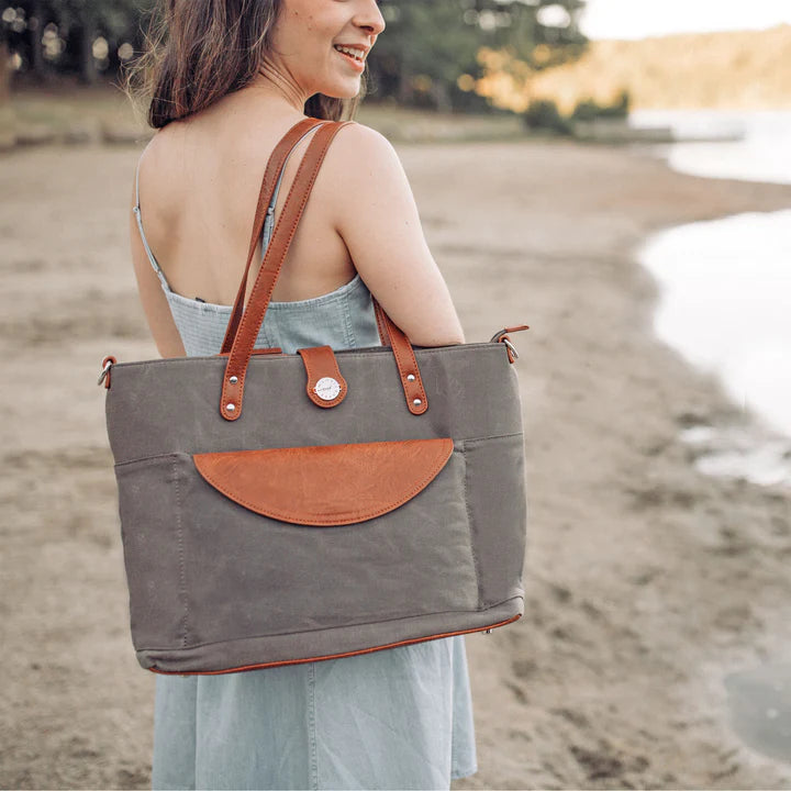 Woman standing next to the beach with the grey carryall travel bag over her shoulder.