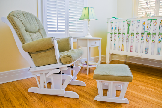 Comfortable white glider rocking chair with green cushions in a home nursery