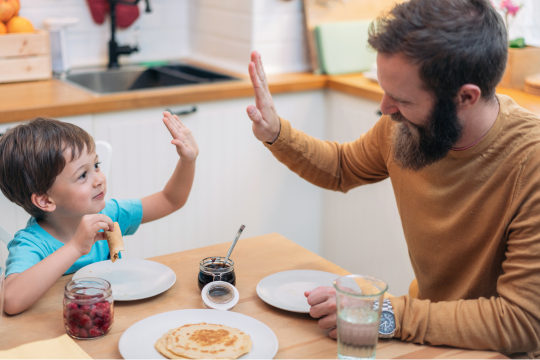 Dad giving his son a high five at the breakfast table