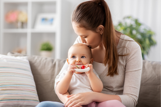 Mom kissing her baby on the head while he chews on a teething toy