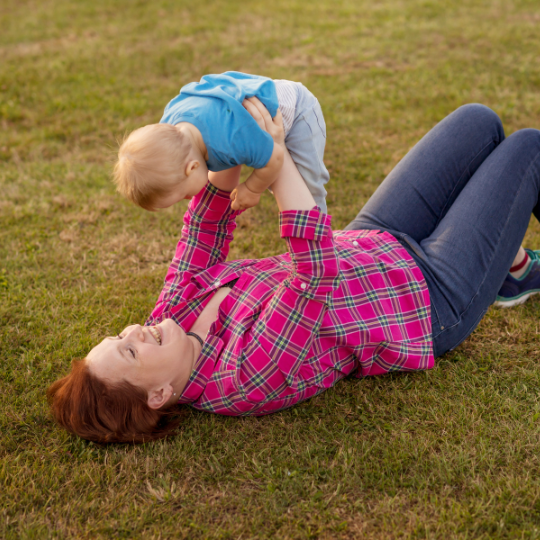 mom laying in grass holding her baby above her chest