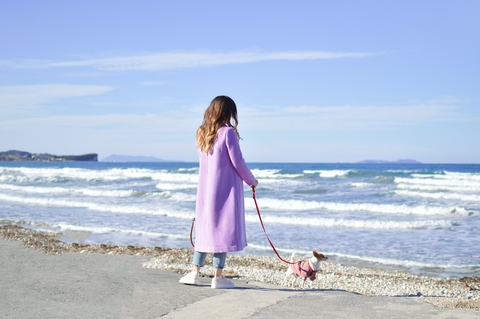 Frau in fider Mantel geht mir Ihrem Hund am Strand spazieren. 
