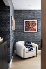 bold navy and wite wall paper with bright art piece and cozy, textured chair