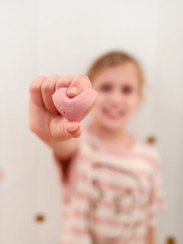 Biting into pink, heart shaped, natural peanut butter cup. 