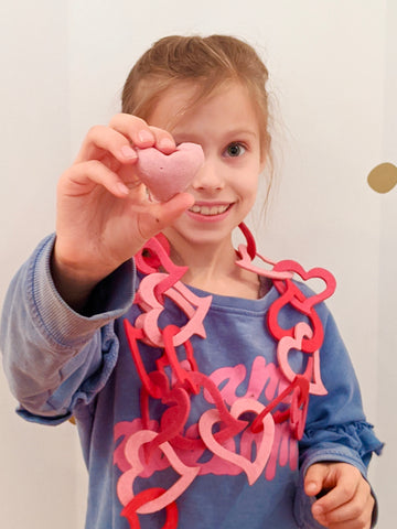 Holding up a pink, heart shaped, natural peanut butter cup. 