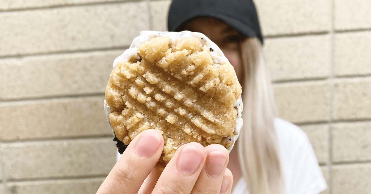 Person Holding Up Peanut Butter Cookie Ice Cream Sandwhich, outside, in front of brick wall