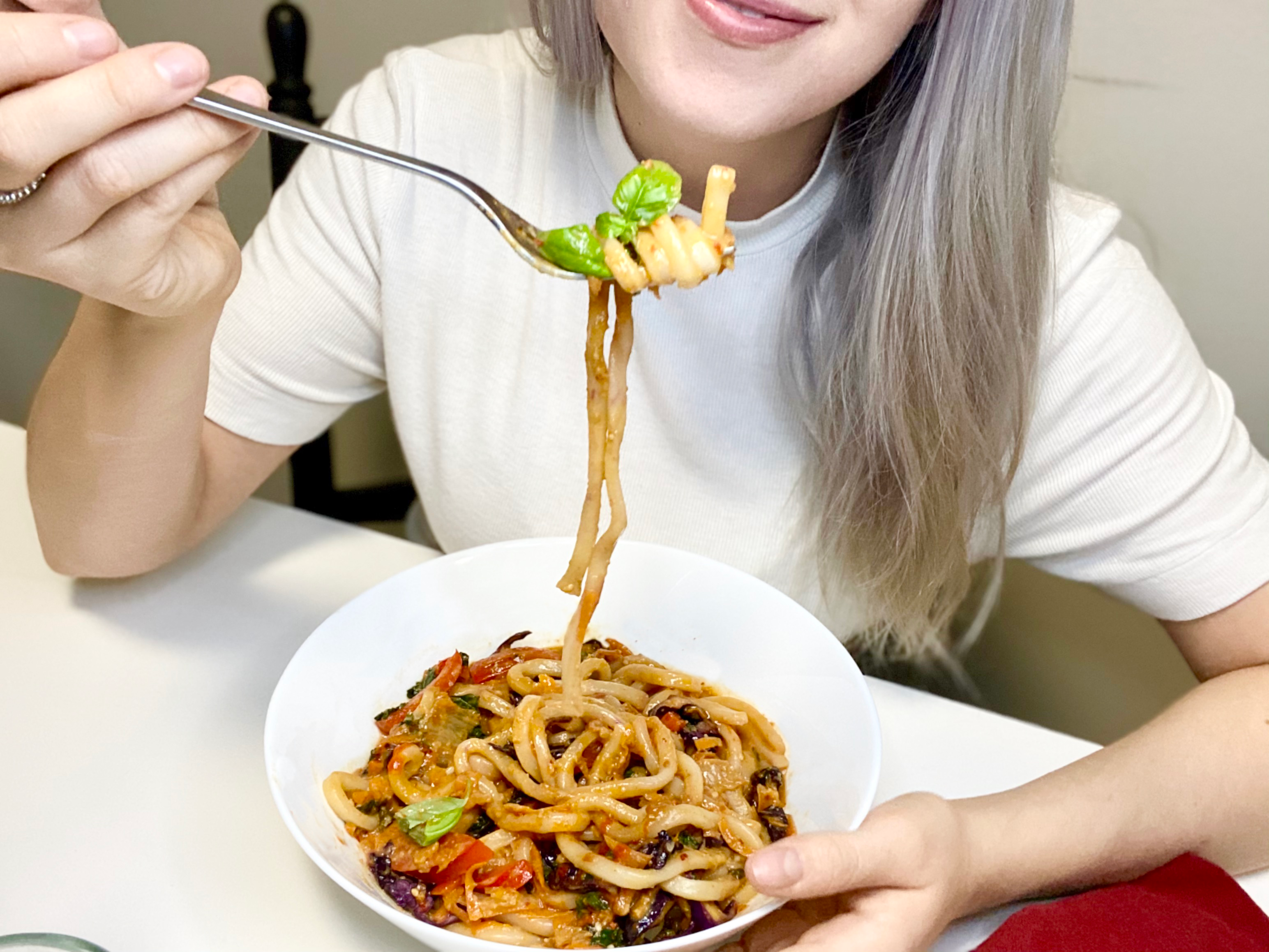 Person smiling and eating noodle bowl filled with veggies and a natural peanut butter sauce.