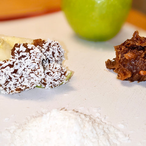 Sliced apple with natural peanut butter caramel date sauce spread, sprinkled with coconut shavings on top. 