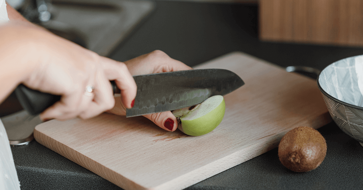 Green apple on cutting board being sliced with knife 