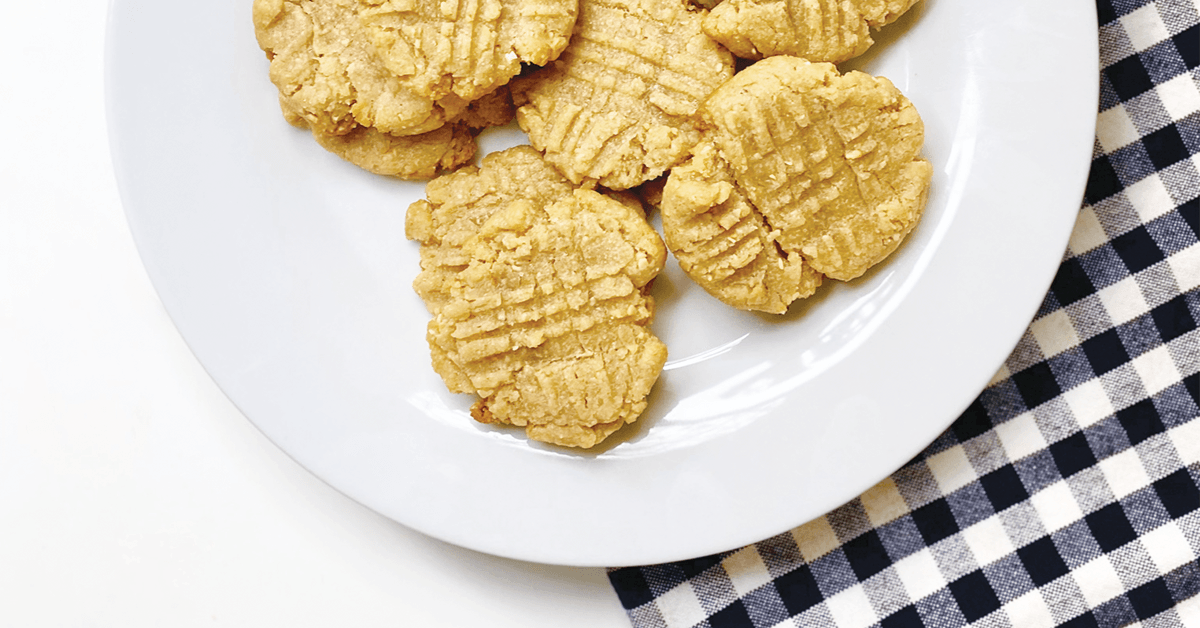 Peanut butter cookies on white plate, resting on black and white checkered cloth. 