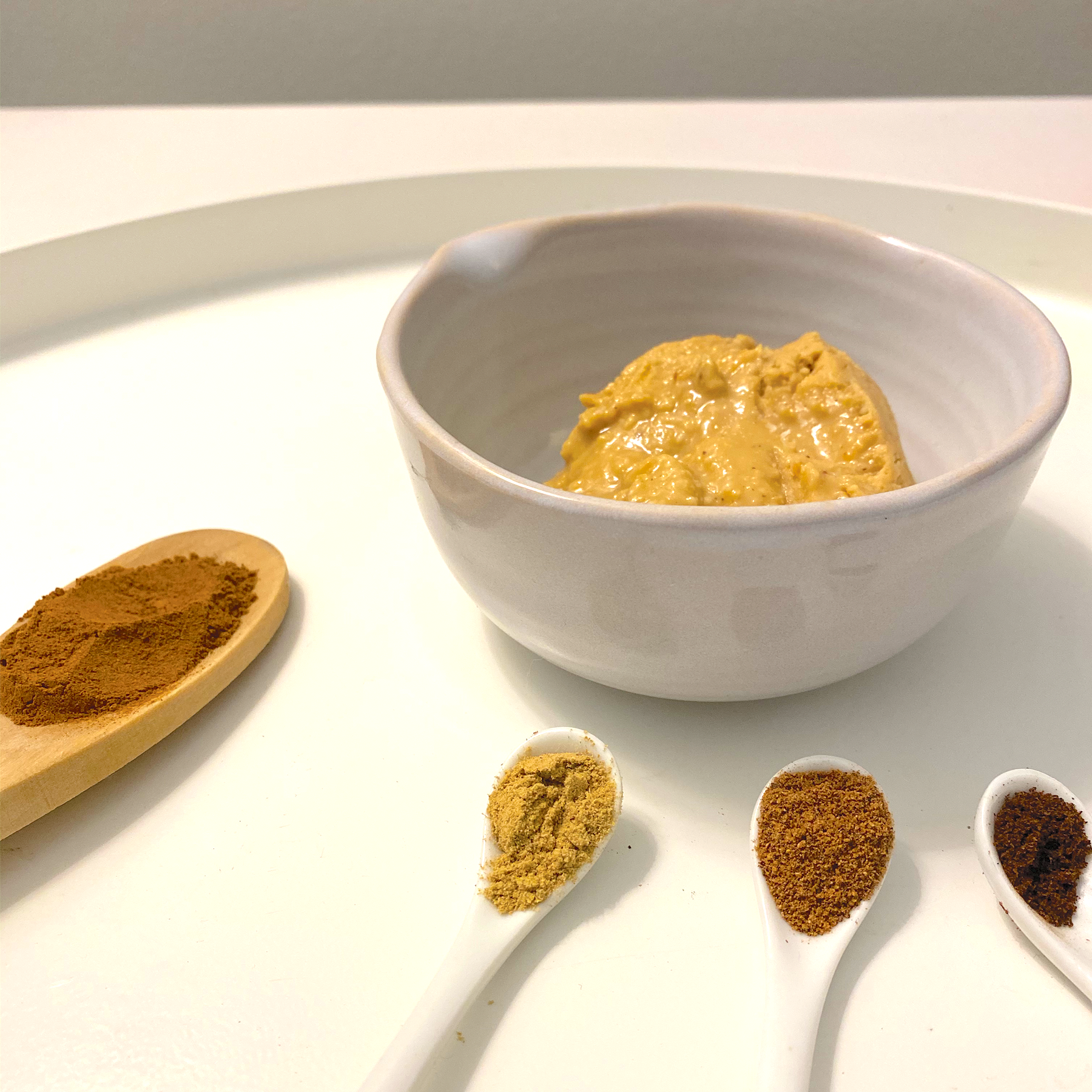 Natural Peanut Butter in a small bowl surrounded by spoons full of spices.