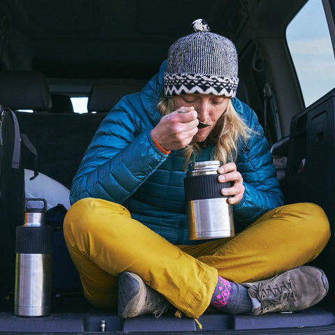 a woman sitting in the open cab, wearning the warm cap, blue jacket and yellow jeans and eating the meal