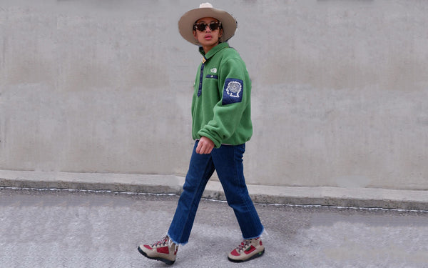 A model posing in the road wearing a green top and blue pants with Supertrek red and beige boots.