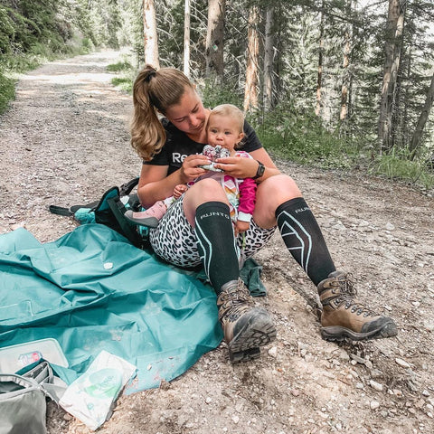 mother wearning the brown joggers and holding the daughter sitting in the forest