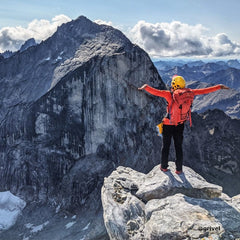 a person is standing on the edge of the mounatin and wearning the yellow helmet