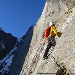  a person wearning the white helmet, yellow jacket, red backpack, black jeans climbing up on the mountaing