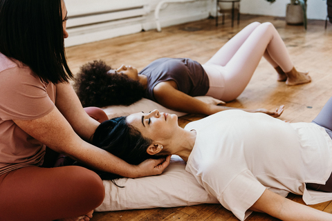 A woman laying down on a mat with a massage therapist massaging neck 
