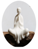 Statue moine bouddhiste zen céramique blanche pose anjali mudra assis sur banc en bois et fond gris Kaosix
