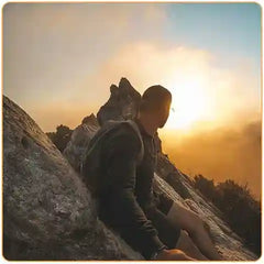 Un homme assis au sommet d'une montagne qui regarde le coucher de soleil Kaosix