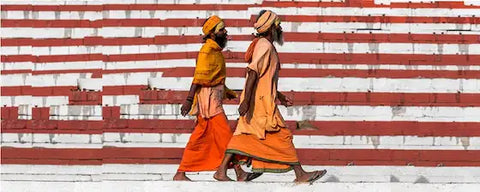deux indiens en robe orange hindouistes marchant le long d'un mur à lignes rouges et blanches Kaosix