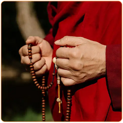 Gros plan sur les mains d'un moine tibétain qui tient un bracelet tibétain en perles de bois kaosix