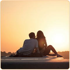 un couple assis sur une dalle de béton qui regarde un coucher de soleil au loin Kaosix