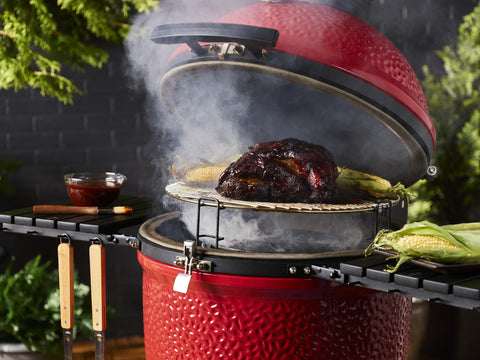 A pork butt and corn on the cob roast on the high rack of a Kamado Joe grill