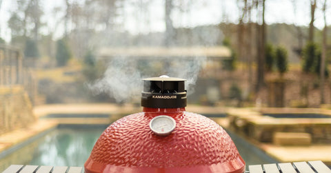 Smoke escapes from the top vent in the dome of a Kamado Joe grill.