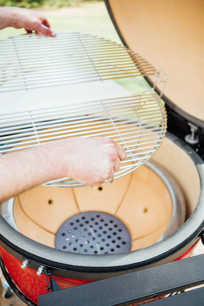 A person uses 2 hands to lift a Divide & Conquer rack with grates out of a Kamado Joe grill