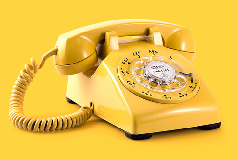 An old-fashioned dialling telephone in bright yellow. The background is also bright yellow