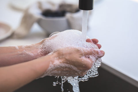 Hands covered in soap being washed under a tap with running water