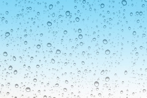 Lots of raindrops running down a glass window. There is a graduated blue in the background