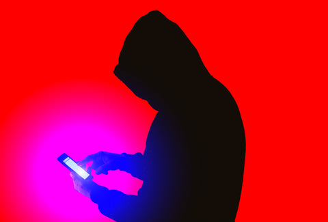 A silhouette of a man holding a mobile phone. The background is bright red signifying danger