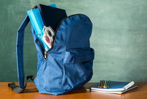 A backpack next to some books. There are some objects inside the backpack – folder, paints