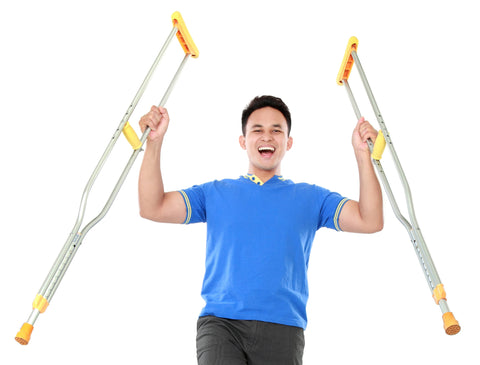 A man looking very happy and holding two crutches in the air