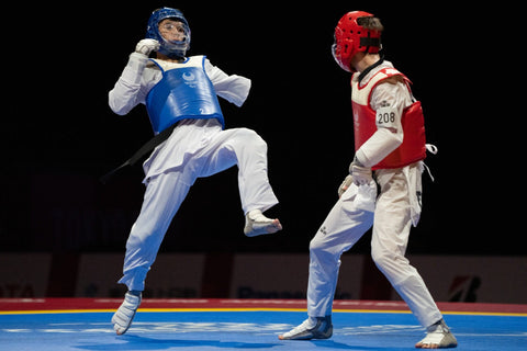 2 Paralympians, one in red protective gear and the other in blue, engaging in a round of taekwondo.