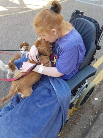 A picture of Ami in her first wheelchair – she is cuddling her dog who hadn't seen her for 6 weeks