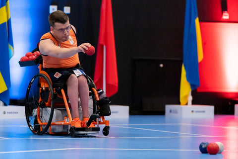 Paralympian about to make a throw with a red Boccia ball.