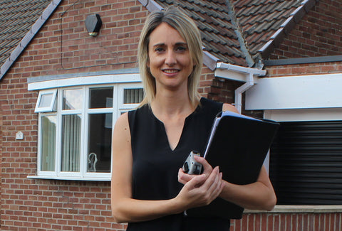 A picture of Kate Makin holding a clip board standing in front of a house
