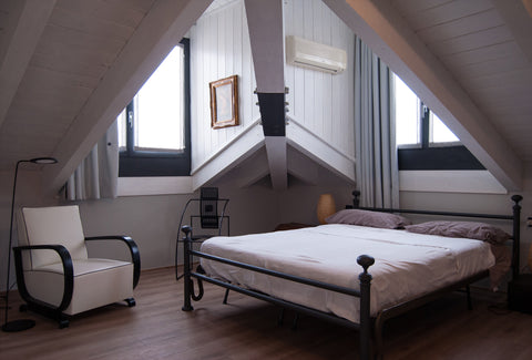 A picture showing a bed that is very close to the ground. The bed is in a room with two windows and a chair