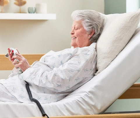 The image is of an elderly woman sitting in the opera classic bed. She is holding the remote control.