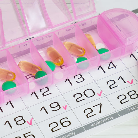 A pink pill box is filled with pills. It's laying on a calendar with several days having been ticked.
