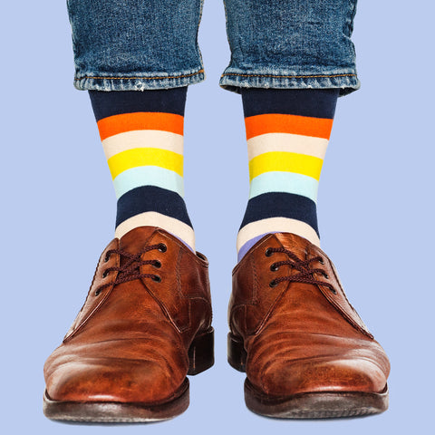A close up of two feet; both have fun, colourful stripy socks on, as well as brown shoes