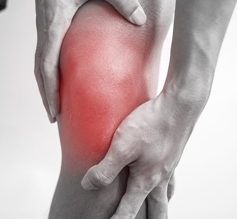 A man's knee – he has both of his hands around the knee. There is a red patch graphic on the knee that suggests the knee is sore and painful