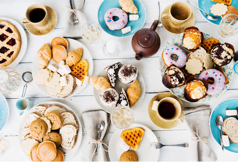 An overhead view of a table that's full of cups of tea, cakes and sandwiches
