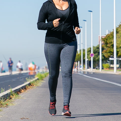 A woman is jogging along the pavement – she is wearing very tight leggings and a top